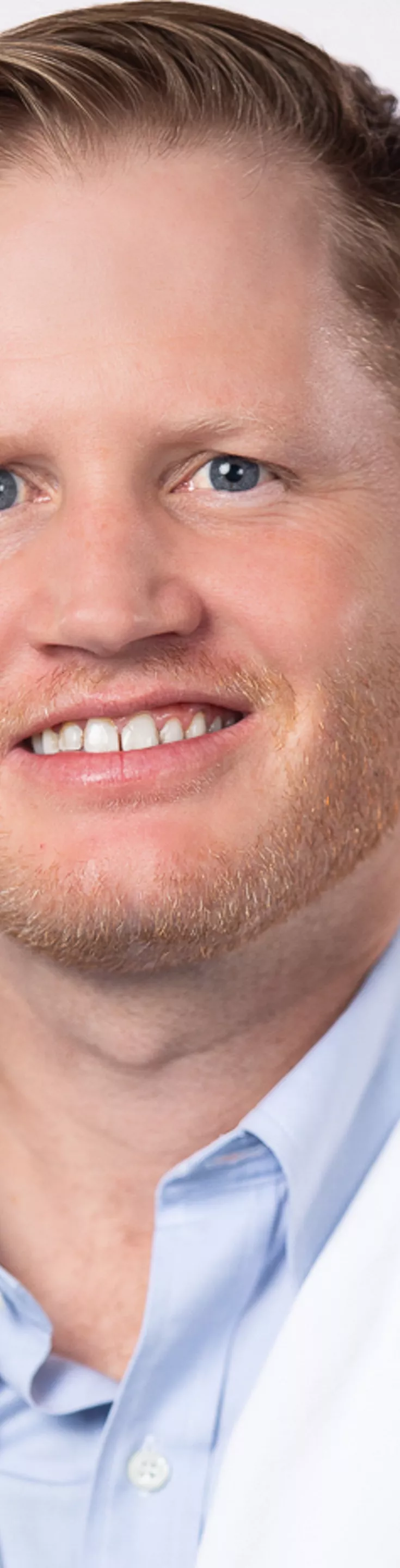 Headshot of Rhett Long. He is wearing a light blue dress shirt and a white coat.