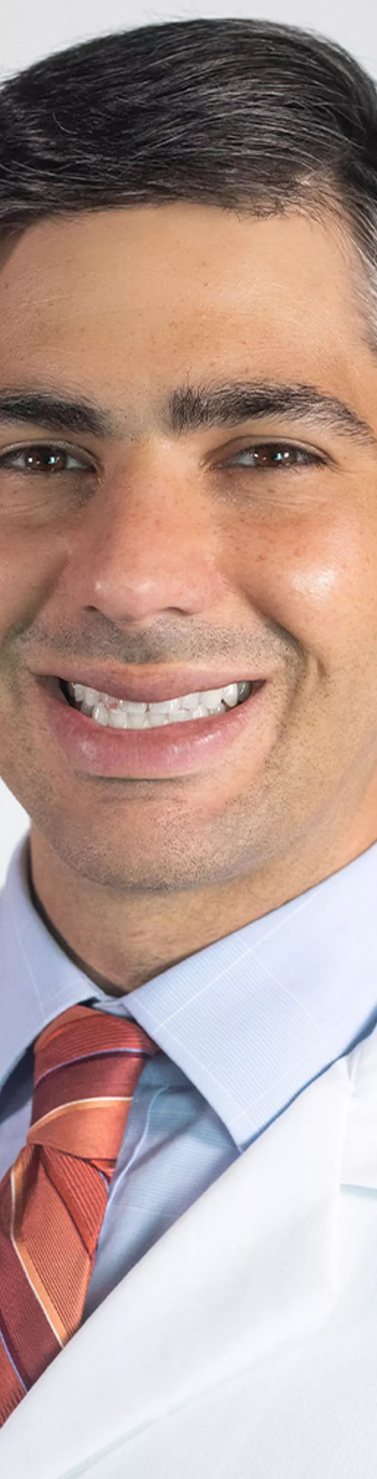 Headshot of Scott Selinger. He is wearing a dress shirt, orange tie, and a white coat.