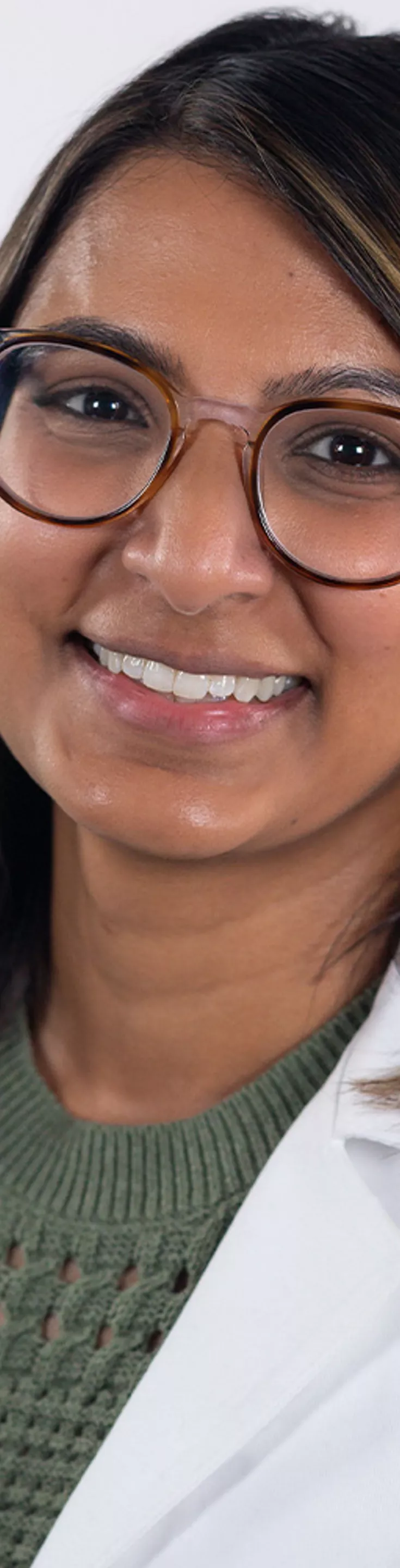 Headshot of Veena Patel. She is wearing an olive green sweater and a white coat.
