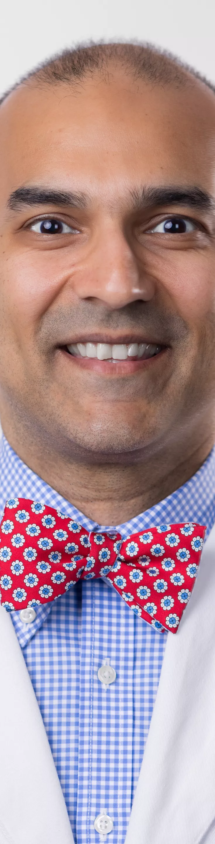 Headshot of Zakariah Mahmood. He is wearing a blue checkered dress shirt, a red bowtie, and a white coat.
