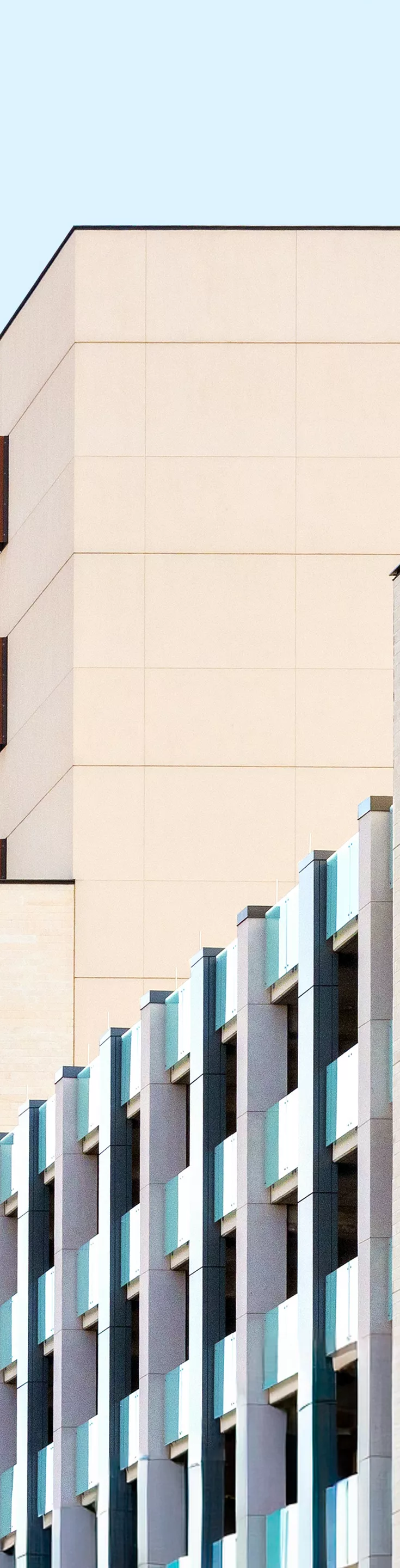 An image of the exterior of the Health Transformation Building (HTB). The image is taken street level a block away. Green foliage is in the foreground and the sky is a light blue.