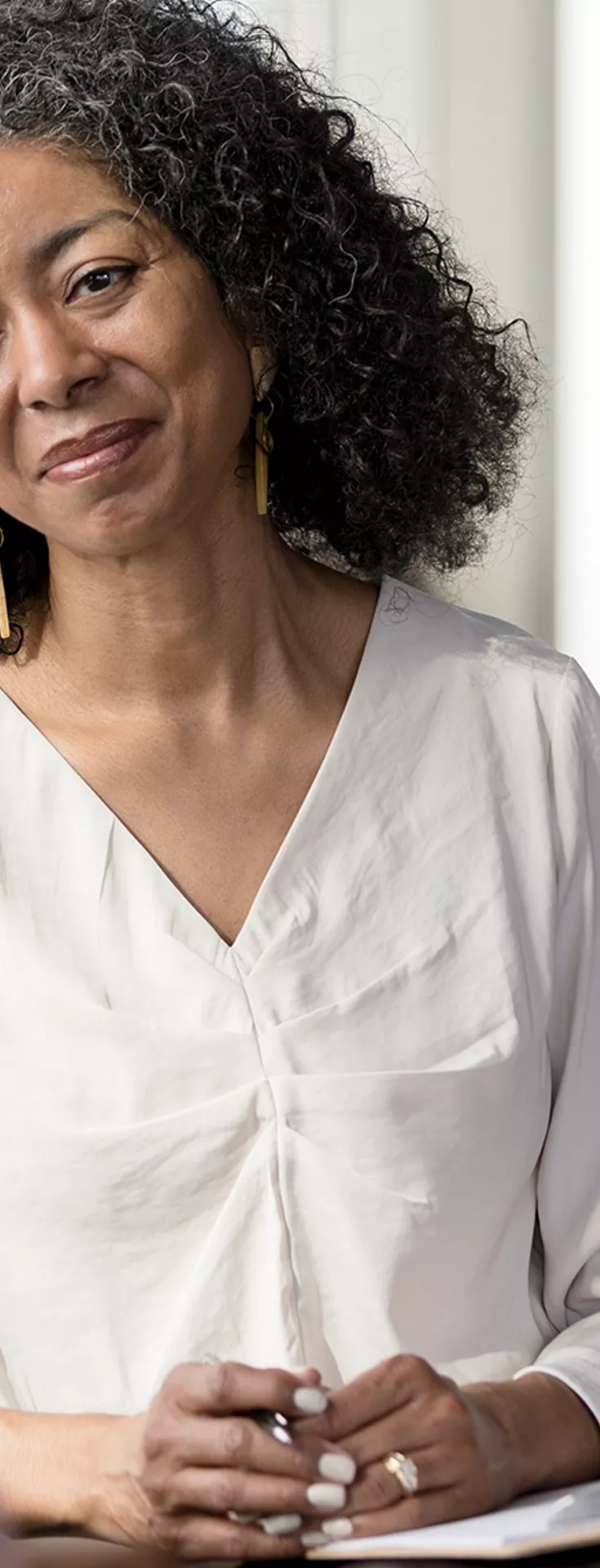 Two women are seated facing each other in a contemporary office environment. One woman holds a clipboard, suggesting a professional or counseling discussion. 