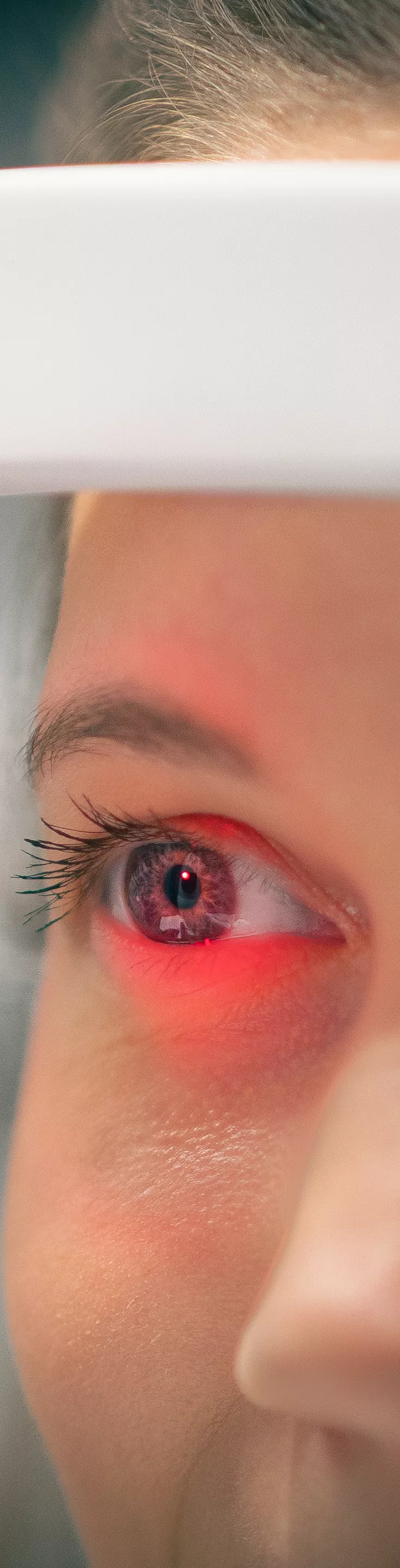 A young woman is seated at an ophthalmology device for an eye examination. The setting appears to be a clinical or optometrist's office, with the focus on the diagnostic equipment. The image highlights the process of vision testing, with the subject's face partially obscured by the machine. The overall mood is clinical and professional, with neutral tones.