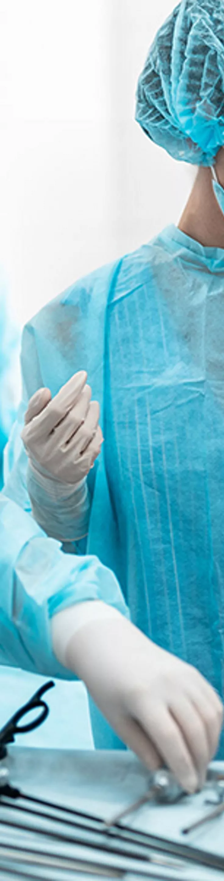 A group of medical professionals in blue surgical gowns and caps are preparing for a procedure in a sterile operating room. Various surgical instruments are neatly arranged on a table, and advanced medical equipment is visible nearby. The environment is clean and clinical, with a focus on precision and teamwork. The scene conveys a sense of professionalism and readiness in a healthcare setting.