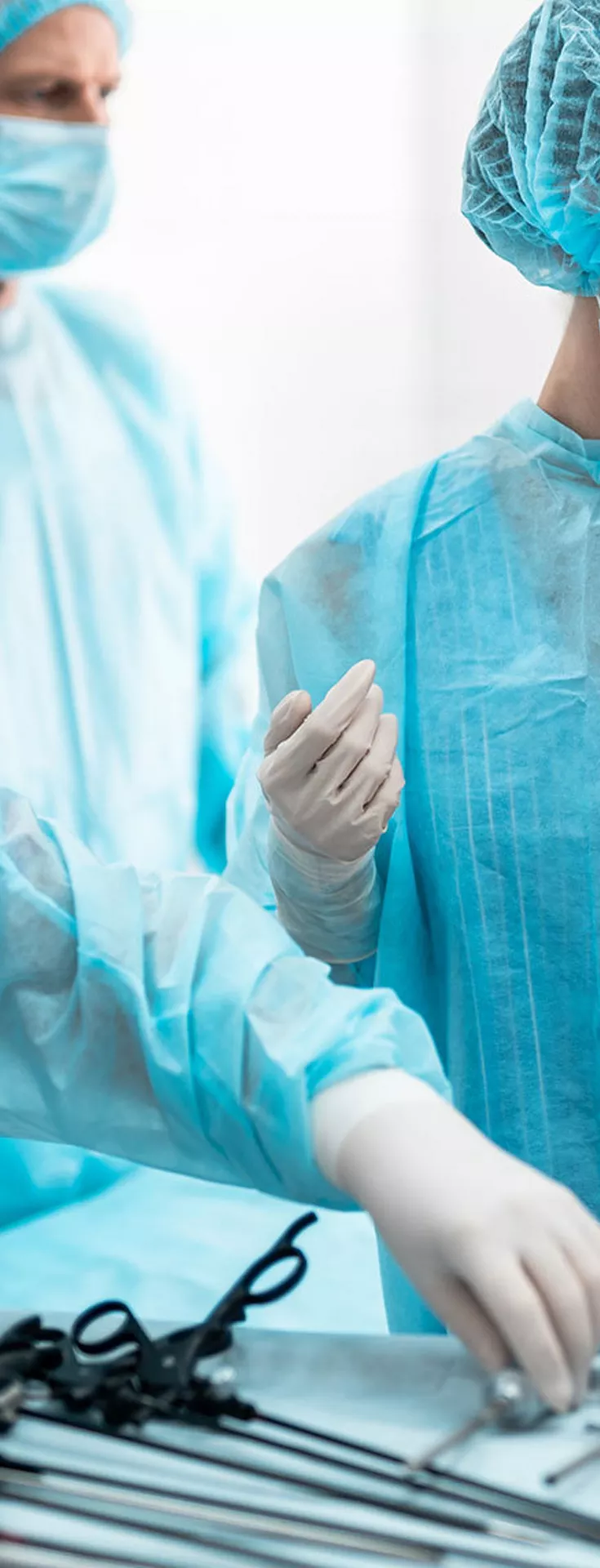 A group of medical professionals in blue surgical gowns and caps are preparing for a procedure in a sterile operating room. Various surgical instruments are neatly arranged on a tray, and advanced medical equipment is visible in the background. 