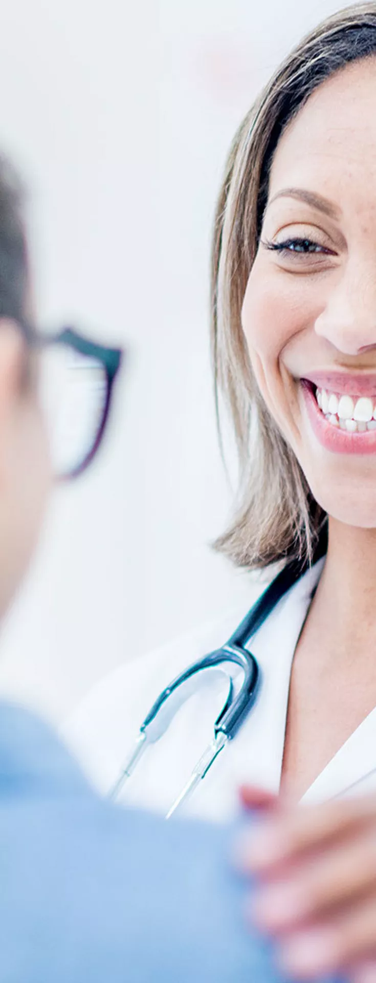 A healthcare professional wearing a white coat and stethoscope gently reassures a patient in a bright, modern medical office. The doctor places a hand on the patient's shoulder, suggesting empathy and support. The scene is well-lit with a soft, neutral color palette, emphasizing a calm and caring atmosphere.