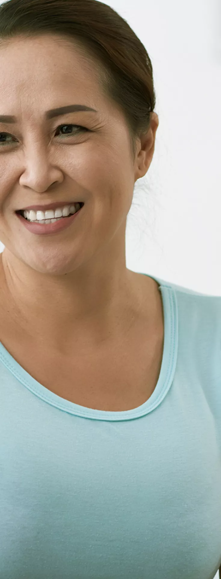 A woman in a light blue shirt sits across from a healthcare professional in a clinical office setting. The professional gently places a hand on the woman's shoulder, suggesting empathy and support. The background features shelves with folders and medical supplies, contributing to a calm and neutral atmosphere. 