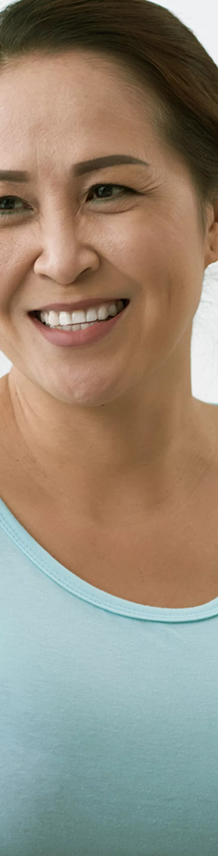 A woman in a light blue shirt sits across from a healthcare professional in a clinical office setting. The professional gently places a hand on the woman's shoulder, suggesting empathy and support. The background features shelves with folders and medical supplies, contributing to a calm and neutral atmosphere. 