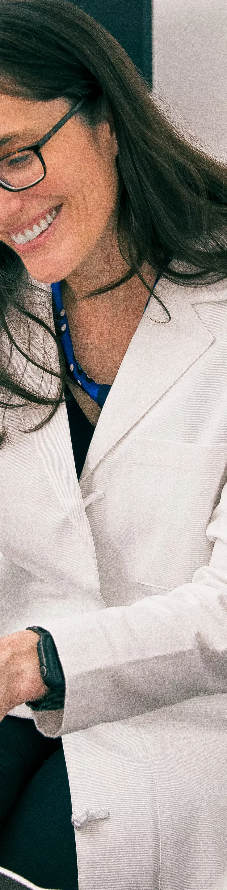 A female doctor in a white coat sits with a patient, examining a series of ultrasound images together. The setting is a modern medical office with neutral tones and a wooden door in the background. Both individuals appear focused and engaged in discussion, suggesting a professional and supportive atmosphere. 