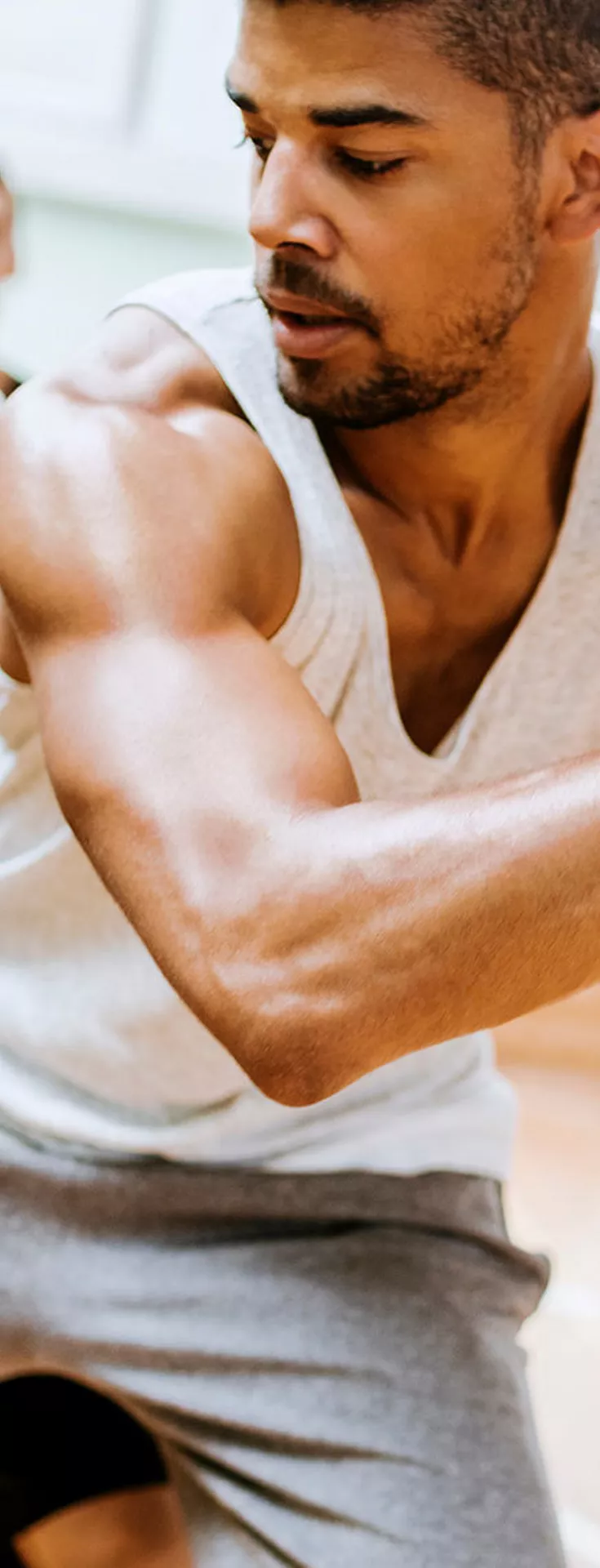 A group of young men are actively playing basketball in an indoor gymnasium. The main subject is holding a basketball, preparing to make a move while being closely guarded by another player. The background shows additional players and a bright, well-lit sports environment. 
