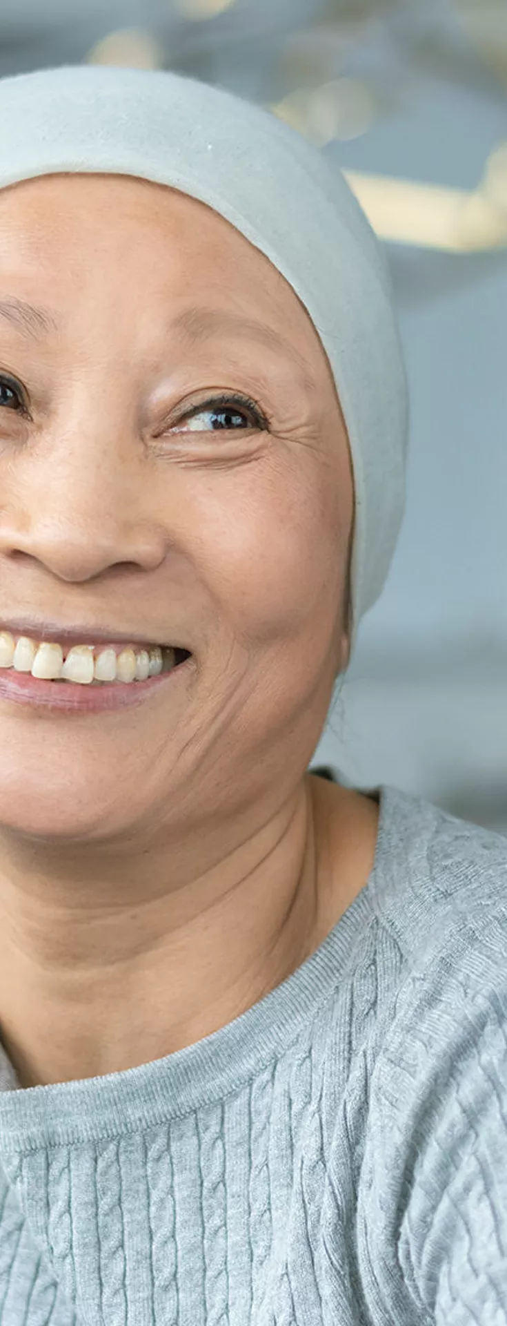 A person wearing a light headscarf and sweater sits across from a medical professional in a modern clinical setting. The two appear to be engaged in a serious conversation, suggesting a healthcare consultation or discussion. 