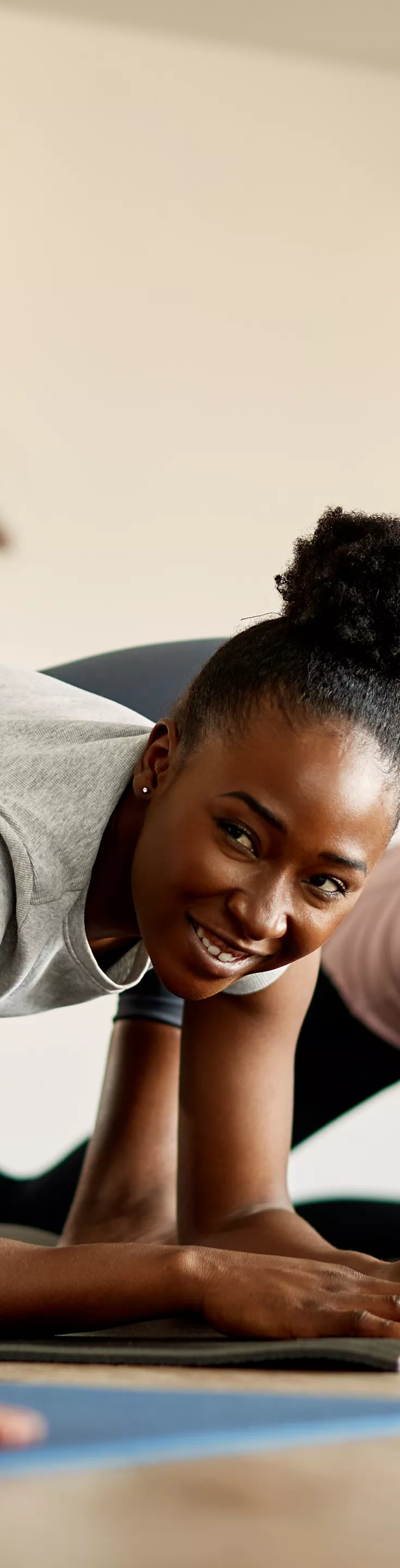 Happy black athletic woman doing stretching exercises with group of women and communicating with one of them during sports training.