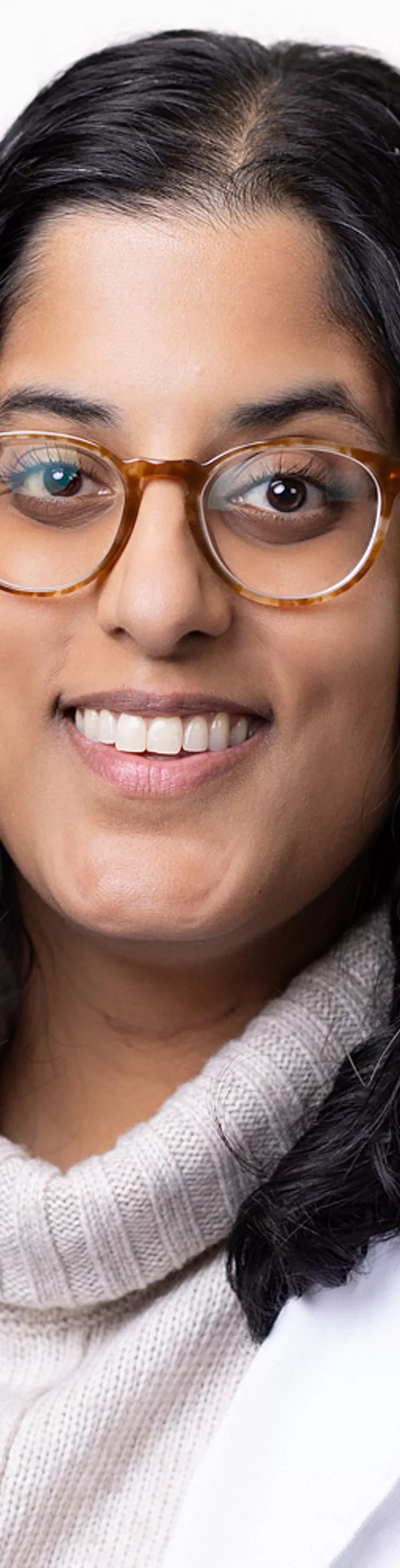 Headshot of Amisha Amin. She is wearing a cream colored and black striped turtleneck sweater with a white coat.