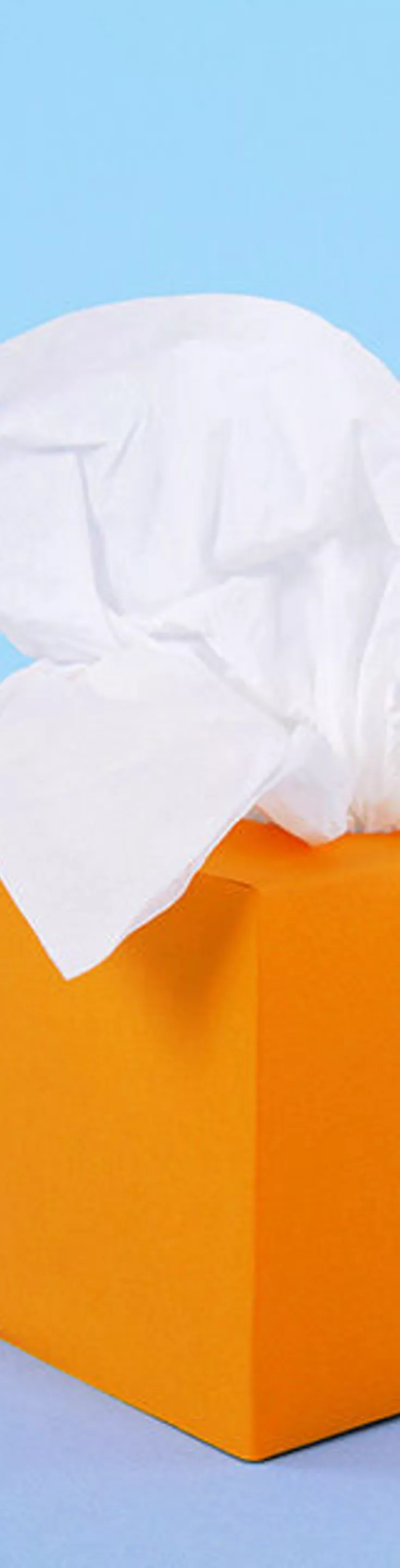 The image features three identical orange tissue boxes, each with white tissues emerging from the top. The boxes are evenly spaced against a solid light blue background, creating a clean and minimalistic visual. The composition highlights the bright color contrast and the soft texture of the tissues. No visible text, numbers, or identifiable brands are present.