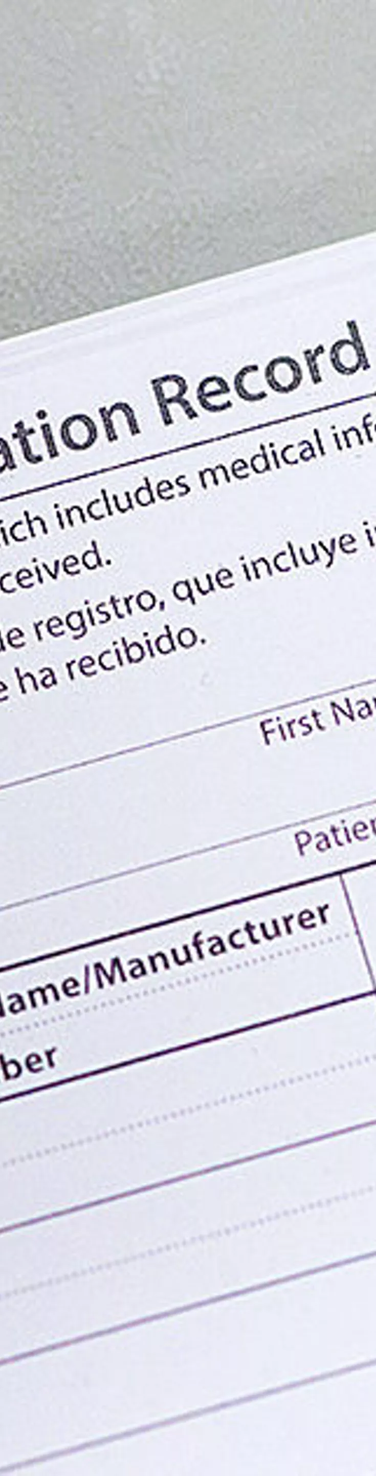 A stack of COVID-19 Vaccination Record Cards is shown on a light-colored table. The card displays fields for vaccine type, product name, manufacturer, lot number, and healthcare professional or clinic site. The CDC logo is clearly visible in the upper right corner. The card includes sections for first and second doses, with date fields formatted as mm/dd/yy. The setting appears clinical and organized, with a neutral color palette.