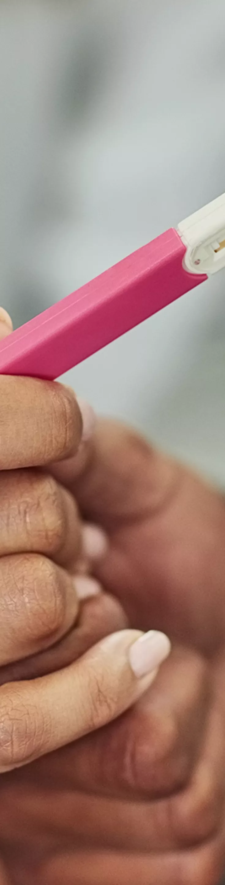 The image shows two people holding a pink and white pregnancy test stick together. The setting appears to be indoors, with the focus on their hands and the test device. The mood is intimate and anticipatory, with soft lighting and neutral tones. 