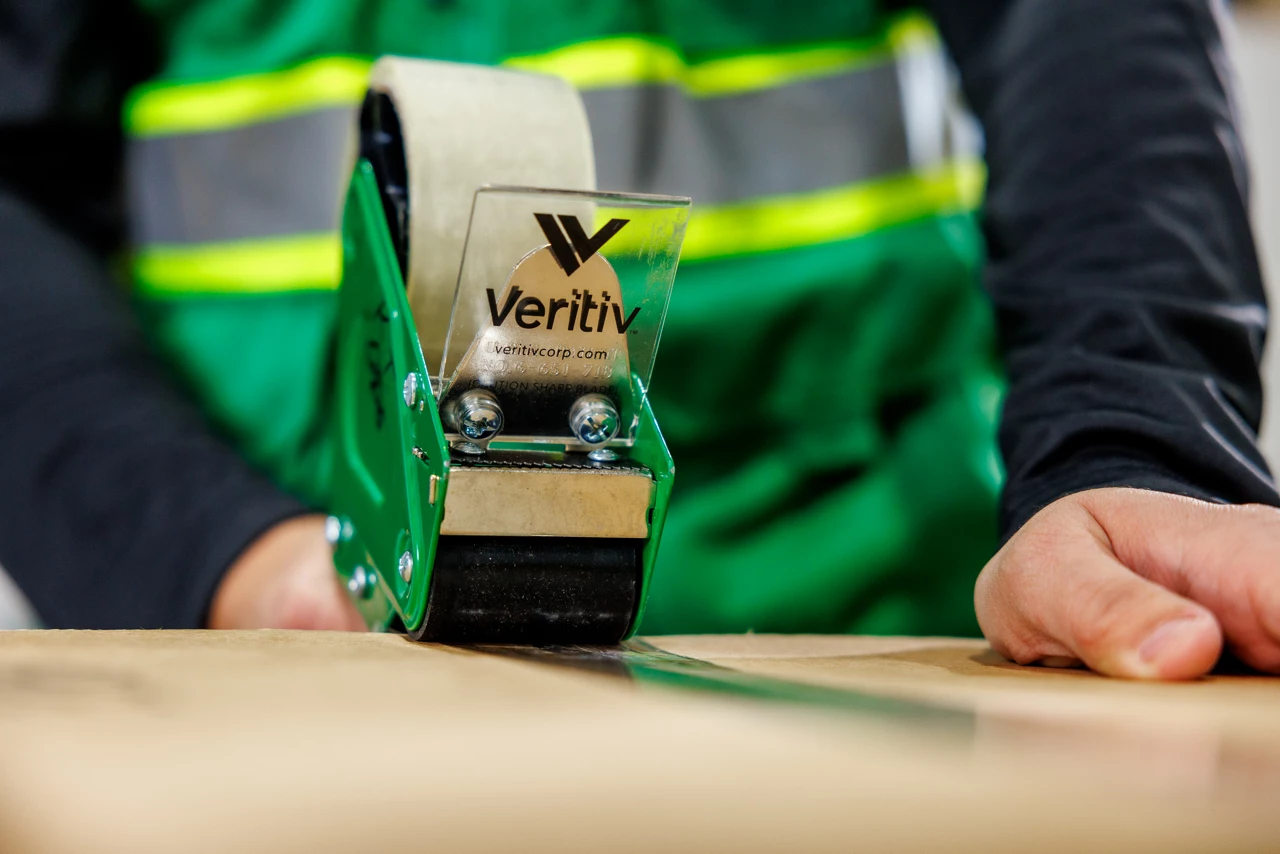 Warehouse worker in green safety vest taping a box shut