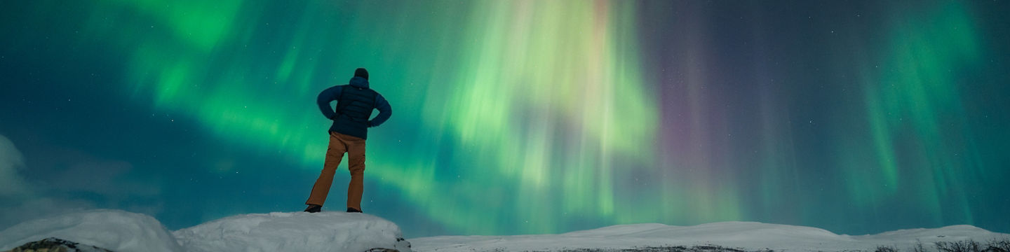 Man watching vibrant northern lights in snow
