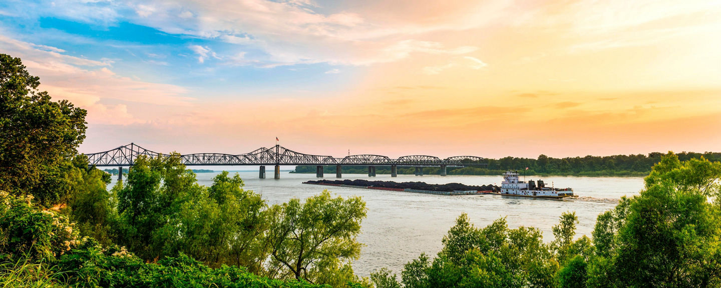 https://s7d9.scene7.com/is/image/viking/Pusher-Boat-Bridge-Sunset-Vicksburg-1%3A5x2-widest?hei=576&wid=1440