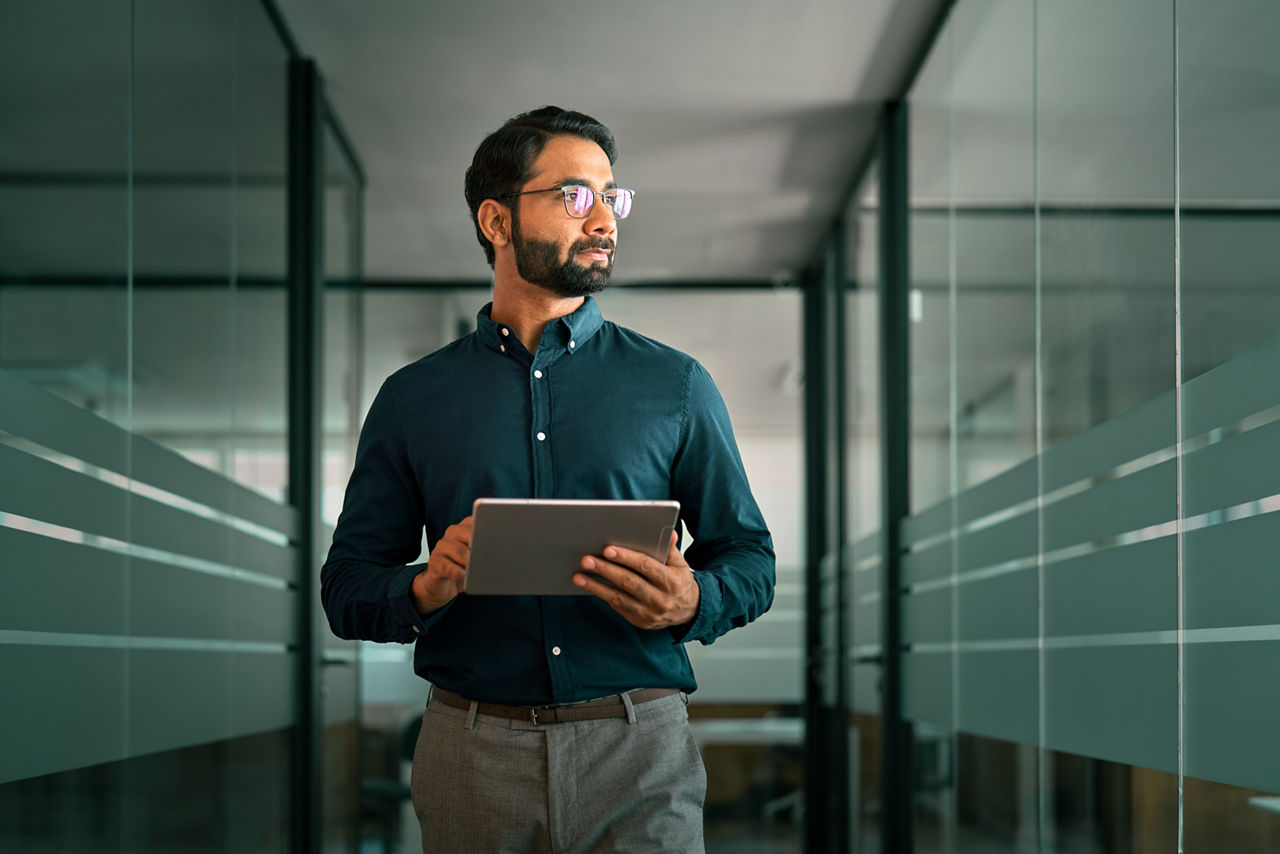 Business man project manager looking away holding digital tablet walking in office. Professional businessman entrepreneur going in hallway holding tab working using tab computer.