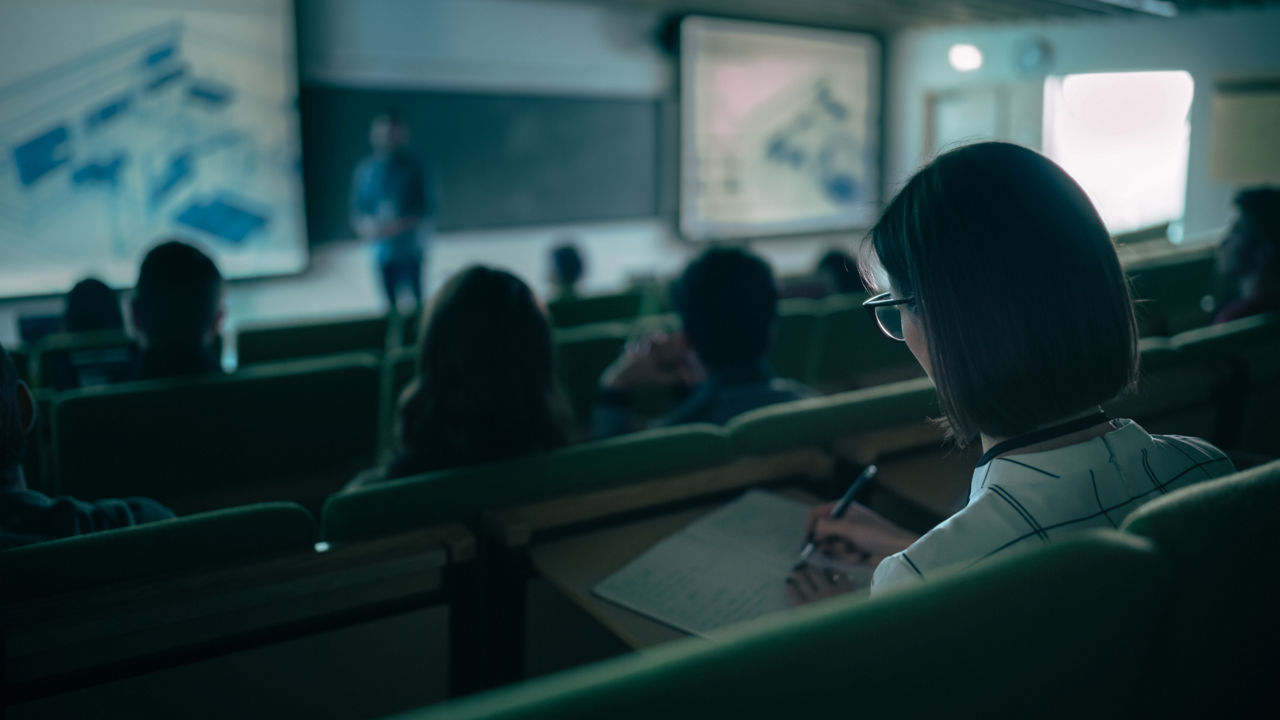 Over the Shoulder Footage of a Female Student Taking Down Notes in a Notebook